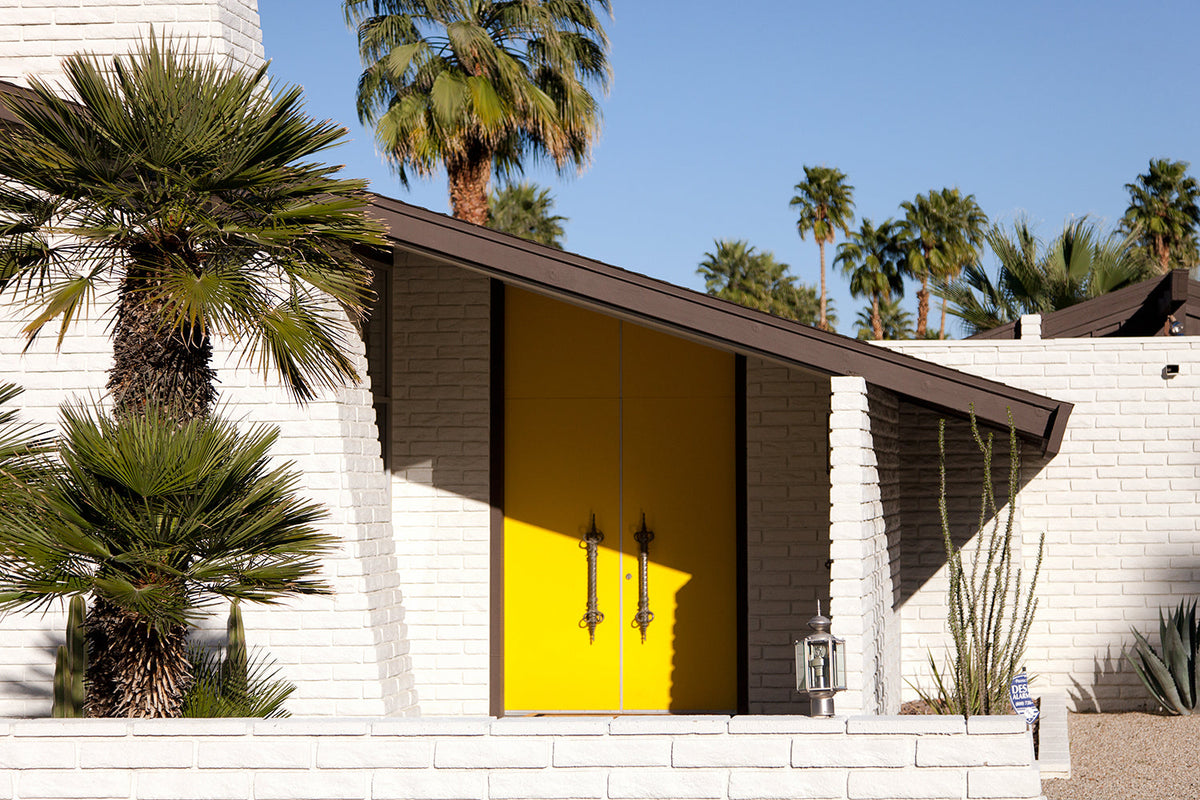 Mid century modern house in Palm Springs with yellow double doors, white brick and palm trees